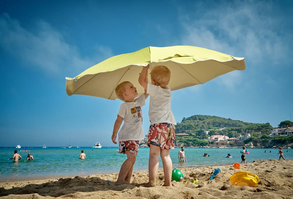 Two kids on the beach setting up a yellow umbrella