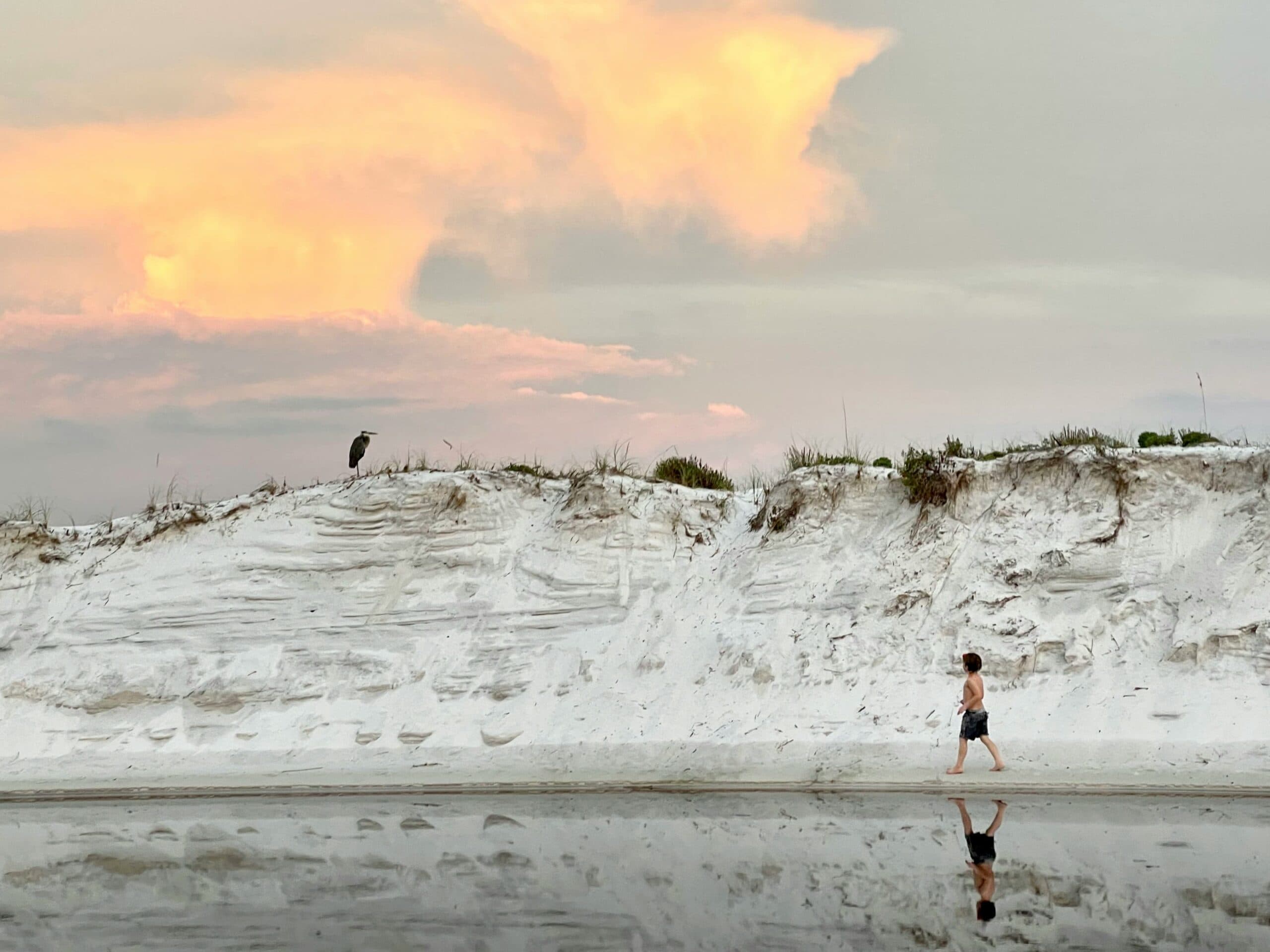Boy walks past a coastal sand dune.
