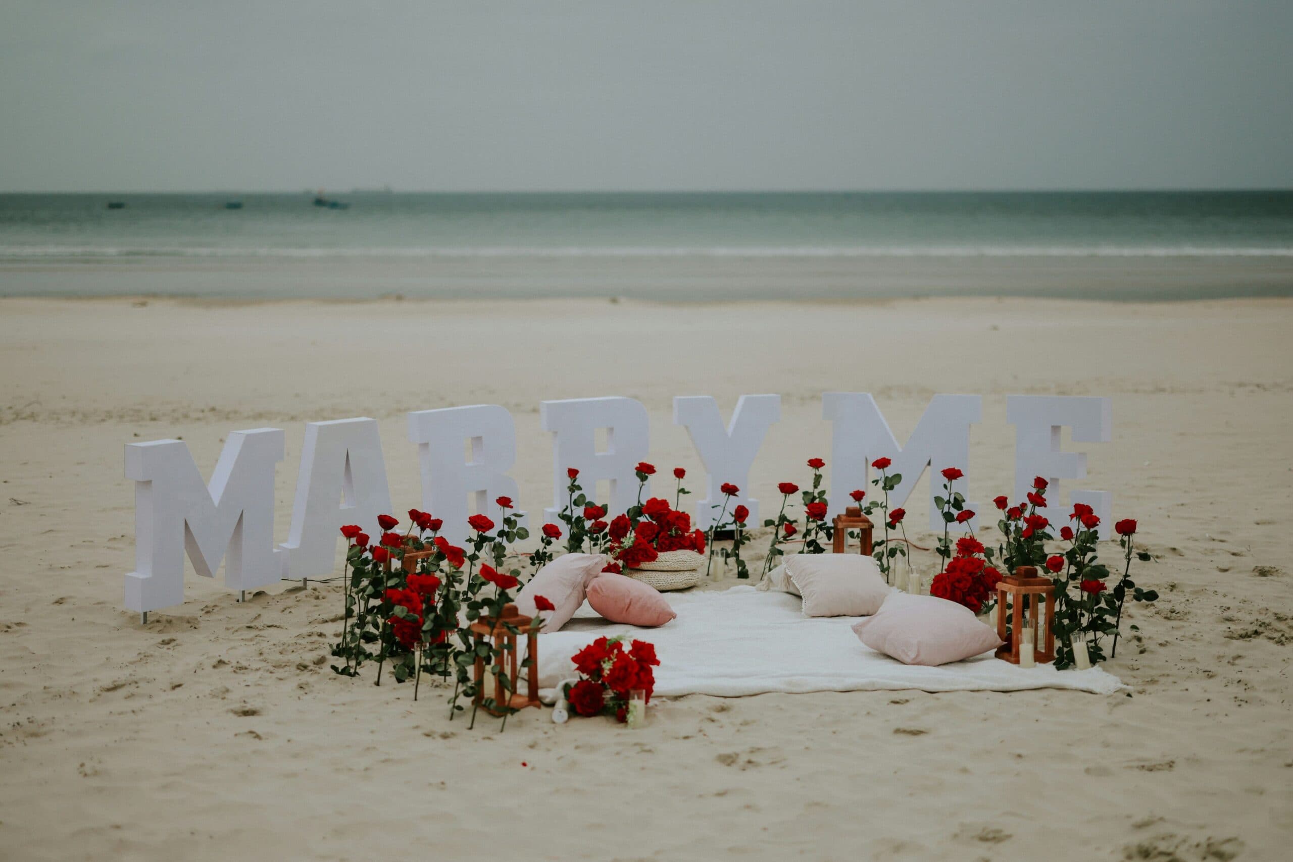 Marry me sign with roses on beach.