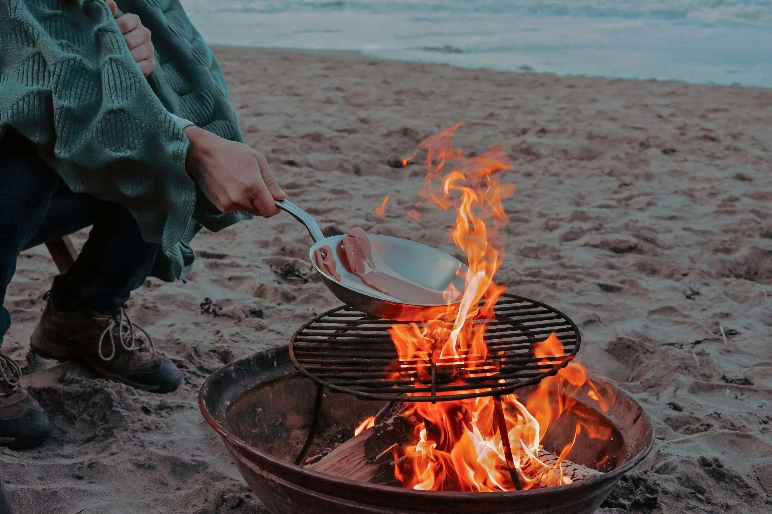 Person cooks food on a fire pit at beach