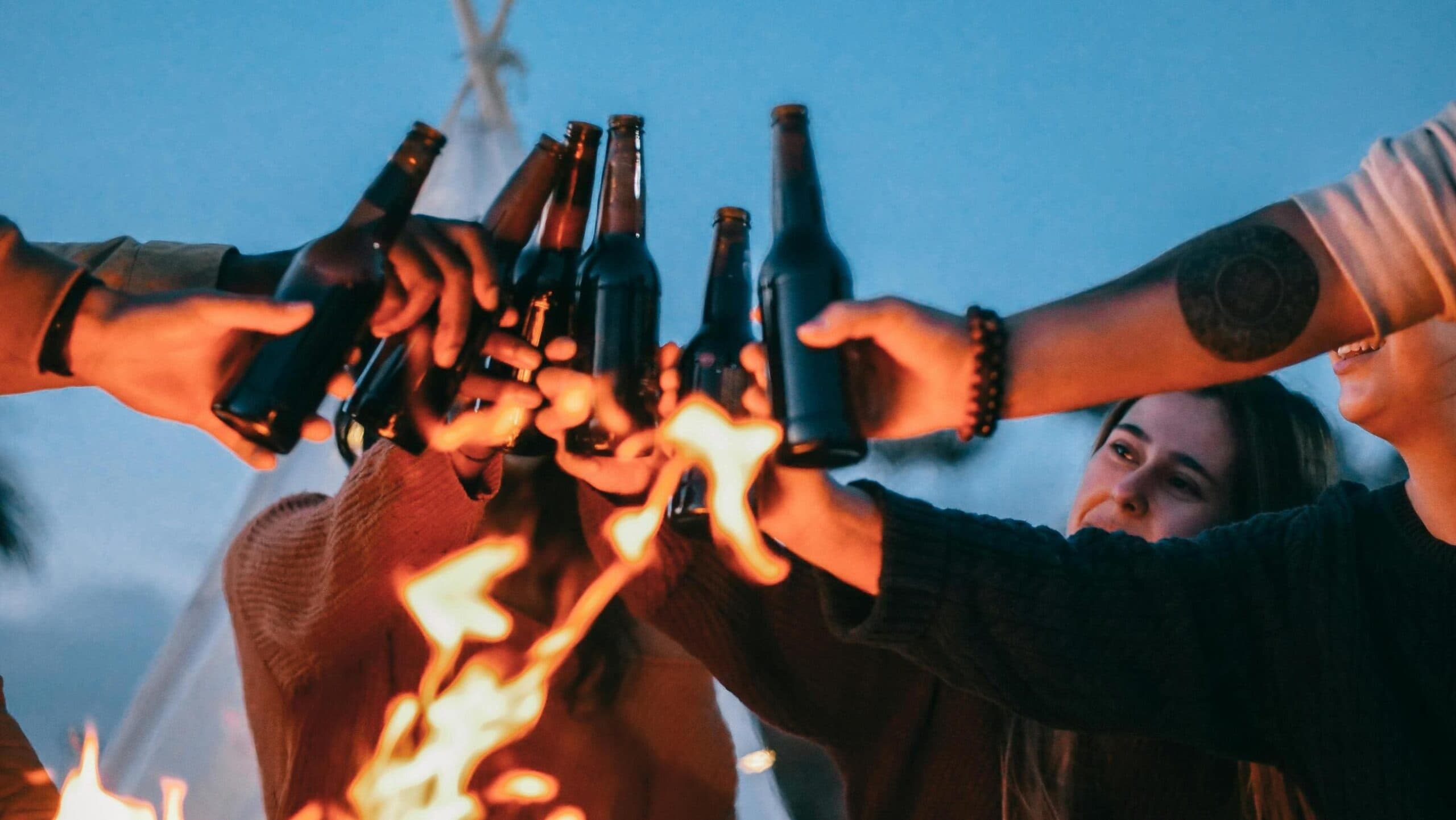 Friends toast beer bottles over a bonfire