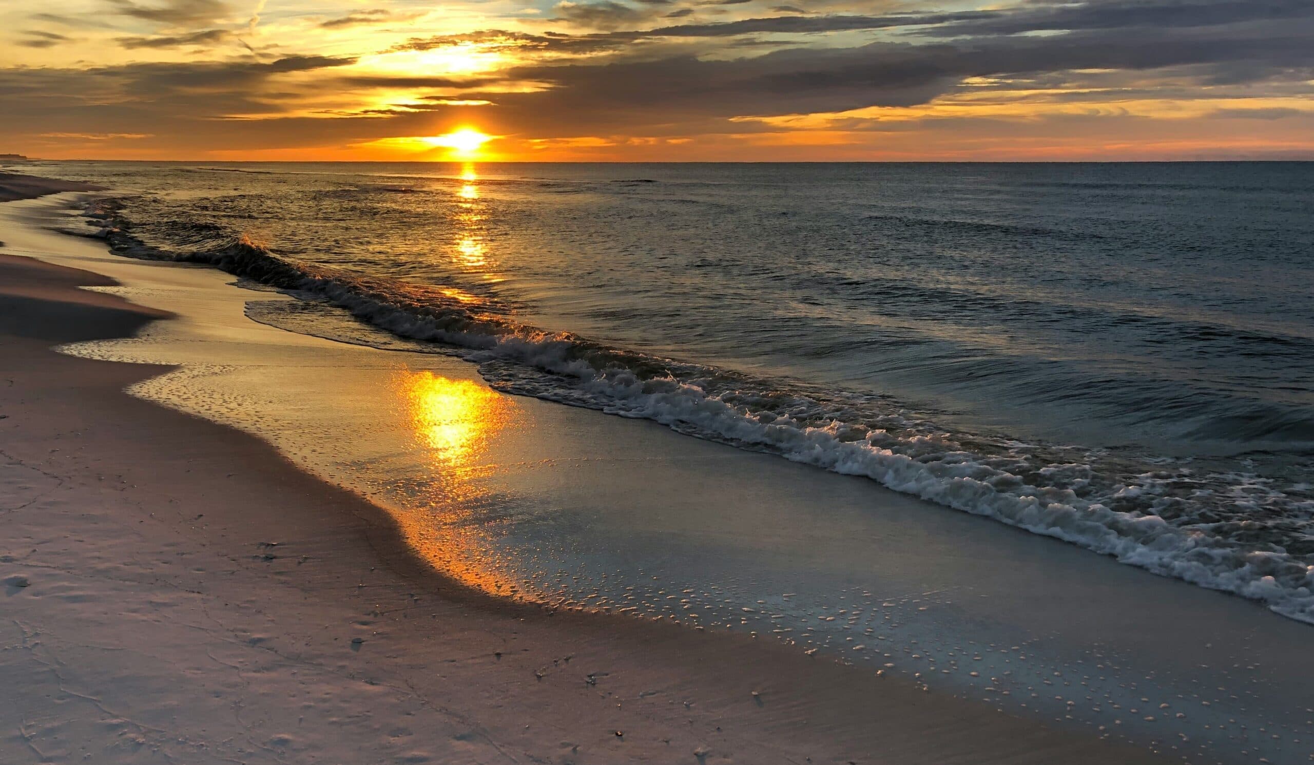 Golden sunset reflects on wet beach sand